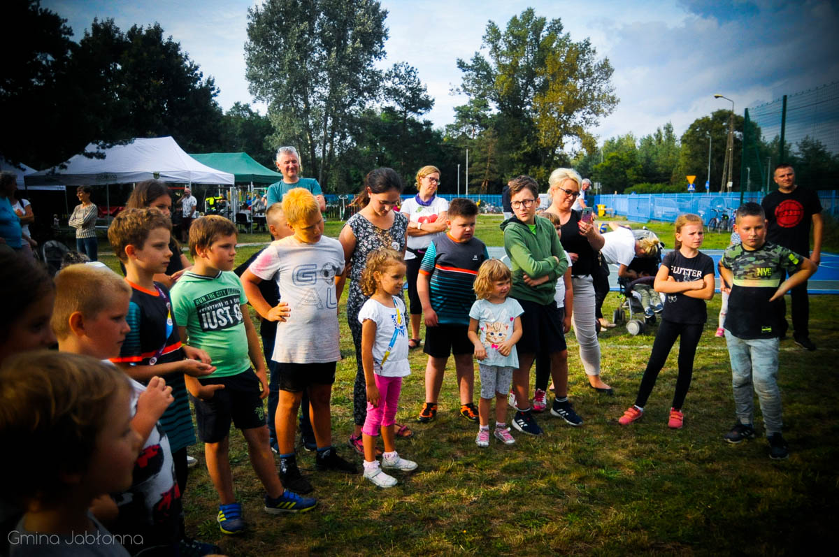 Grupa kilkunastu uśmiechniętych i zaciekawionych dzieci stojących w kręgu. 